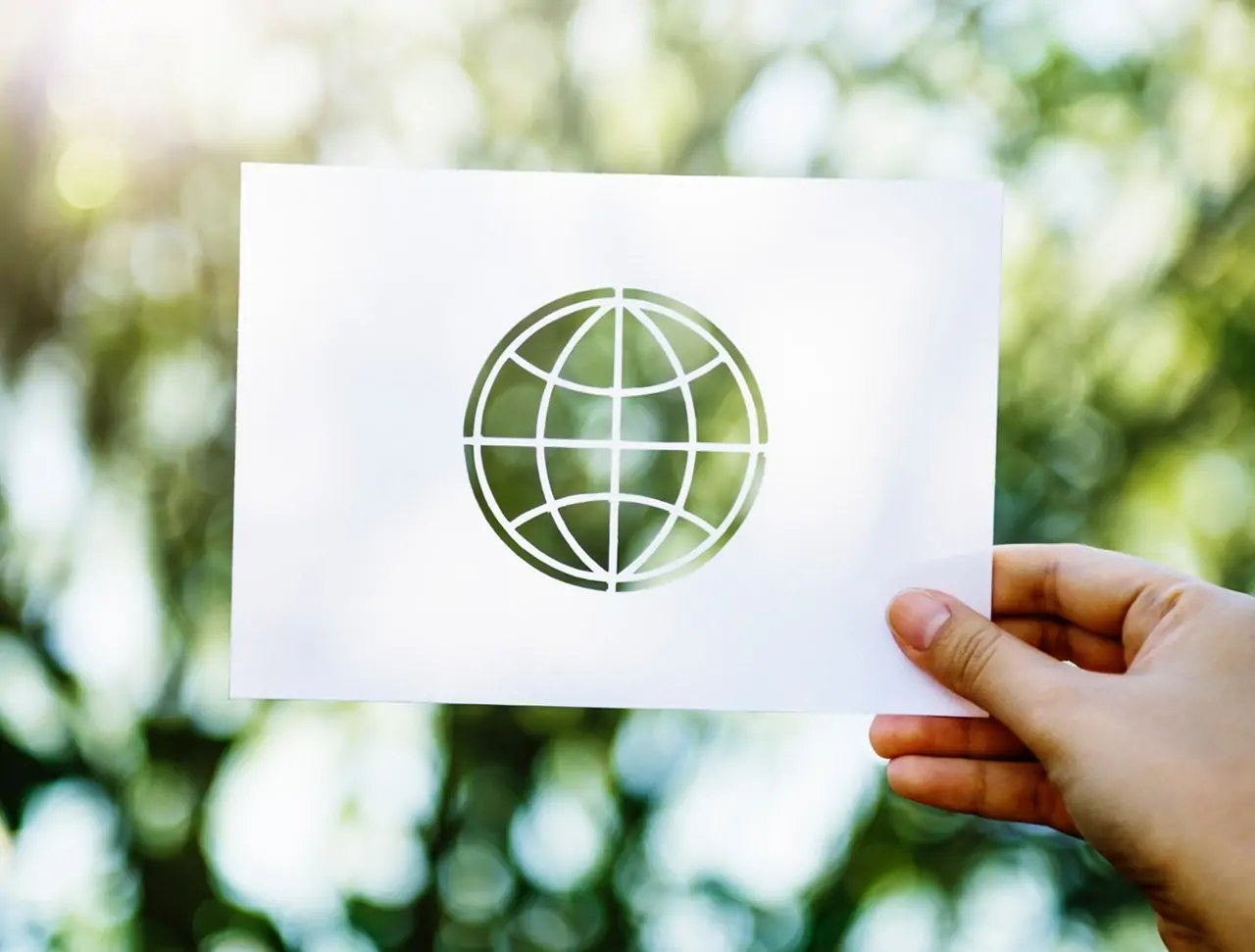 Photo of a person holding up a transparent photo of a global in front of a plant background. 