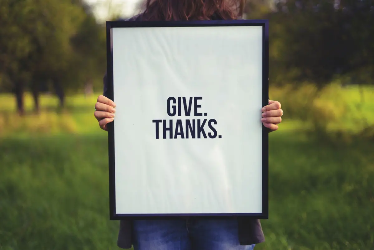 Girl holding a sign that says "Give Thanks" this image is important because when leaders thank their employees it increases motivation and organizational commitment