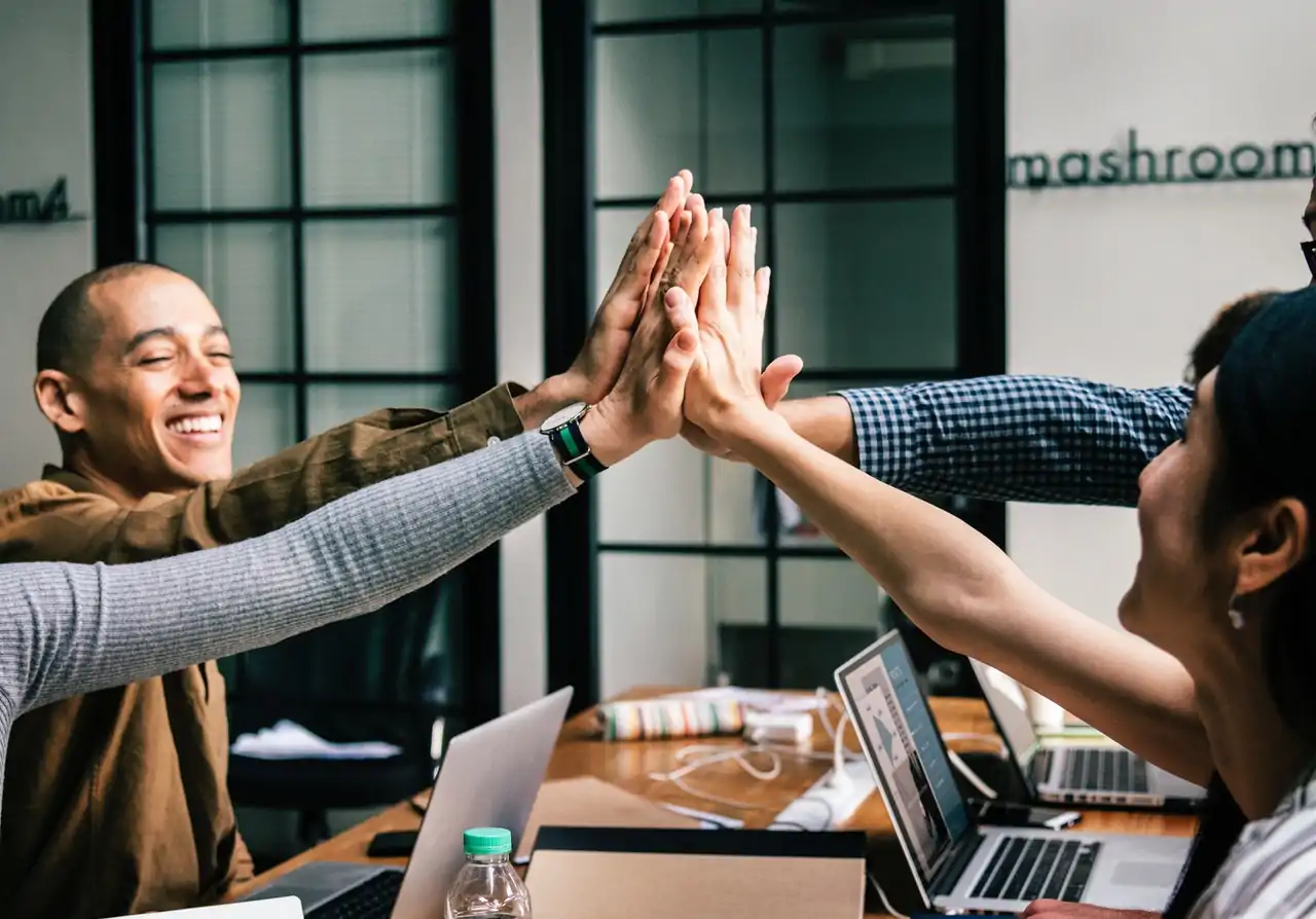 Photo of four engaged employees sitting around a desk and giving each other high fives. 