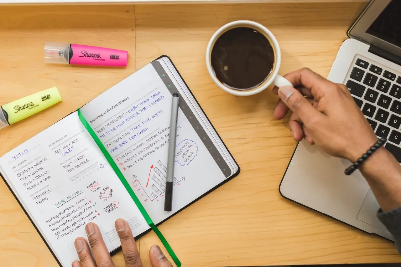 Photo of a person sitting at a desk, drinking a couple of coffee and reviewing their to-do items for the week