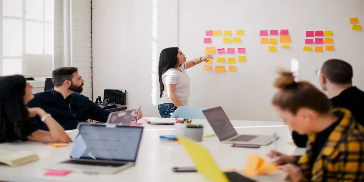 Photo of an employee standing in front  of a whiteboard and explaining what she learned from a recent experiment. 